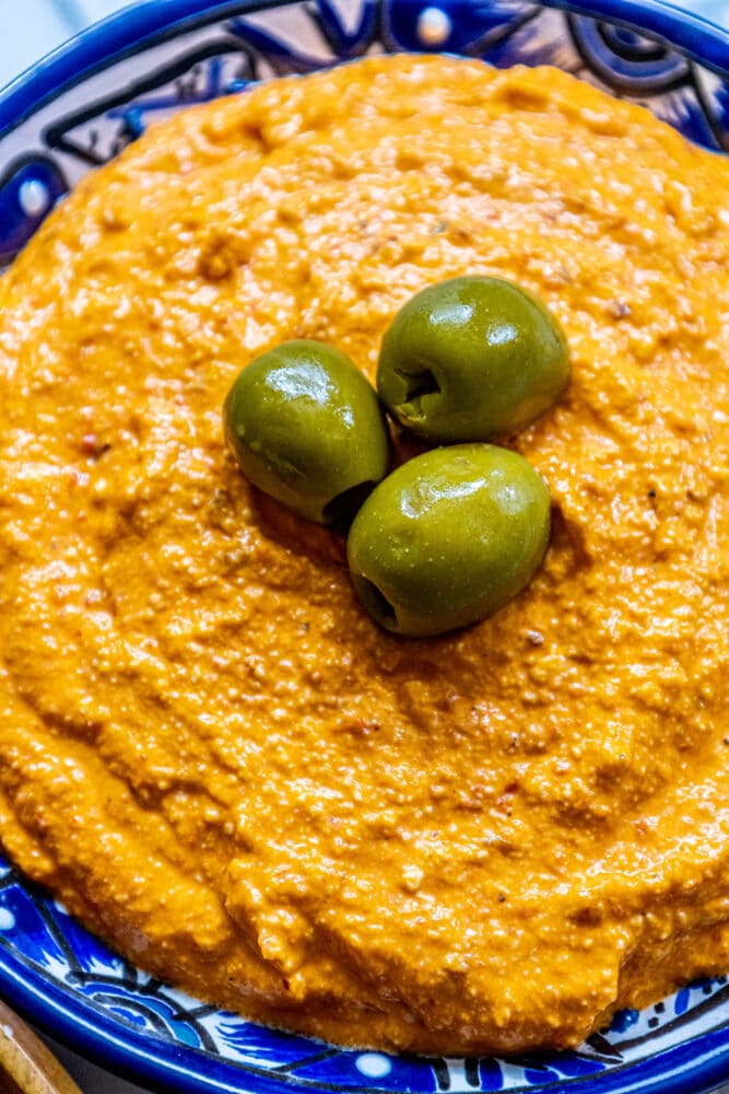 picture of whipped feta cheese dip with three olives on top in a blue bowl next to a bowl of bread and olives on a table