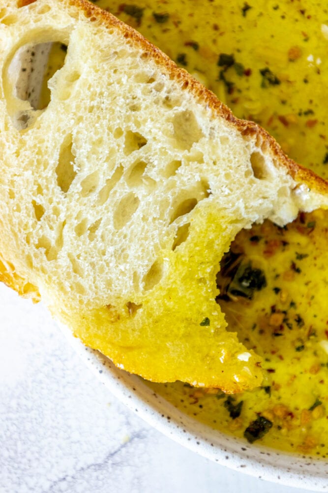 a slice of bread next to a bowl full of olive oil bread dip 