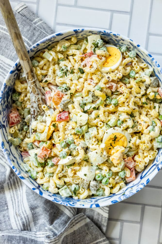 macaroni salad with peppers, peas, mayonnaise, and boiled eggs in a blue bowl