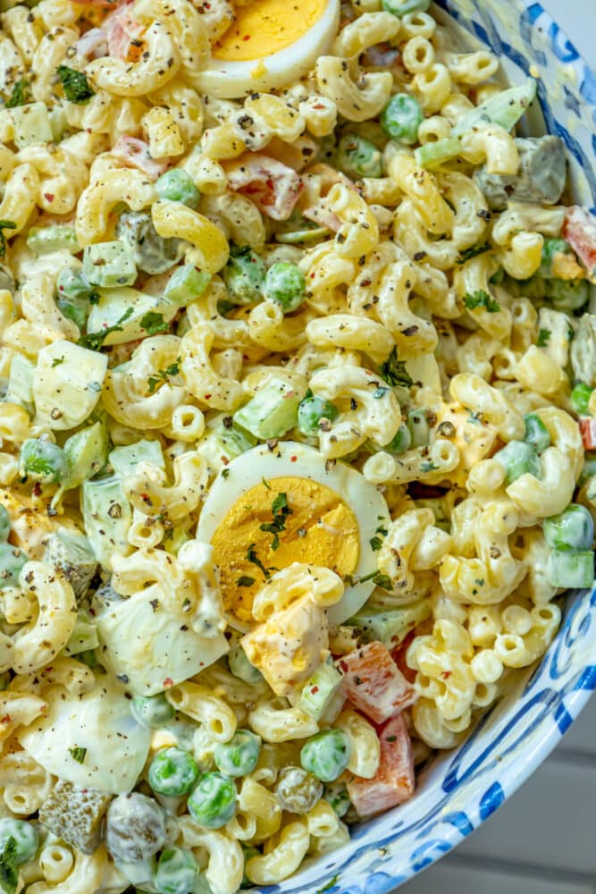macaroni salad with peppers, peas, mayonnaise, and boiled eggs in a blue bowl