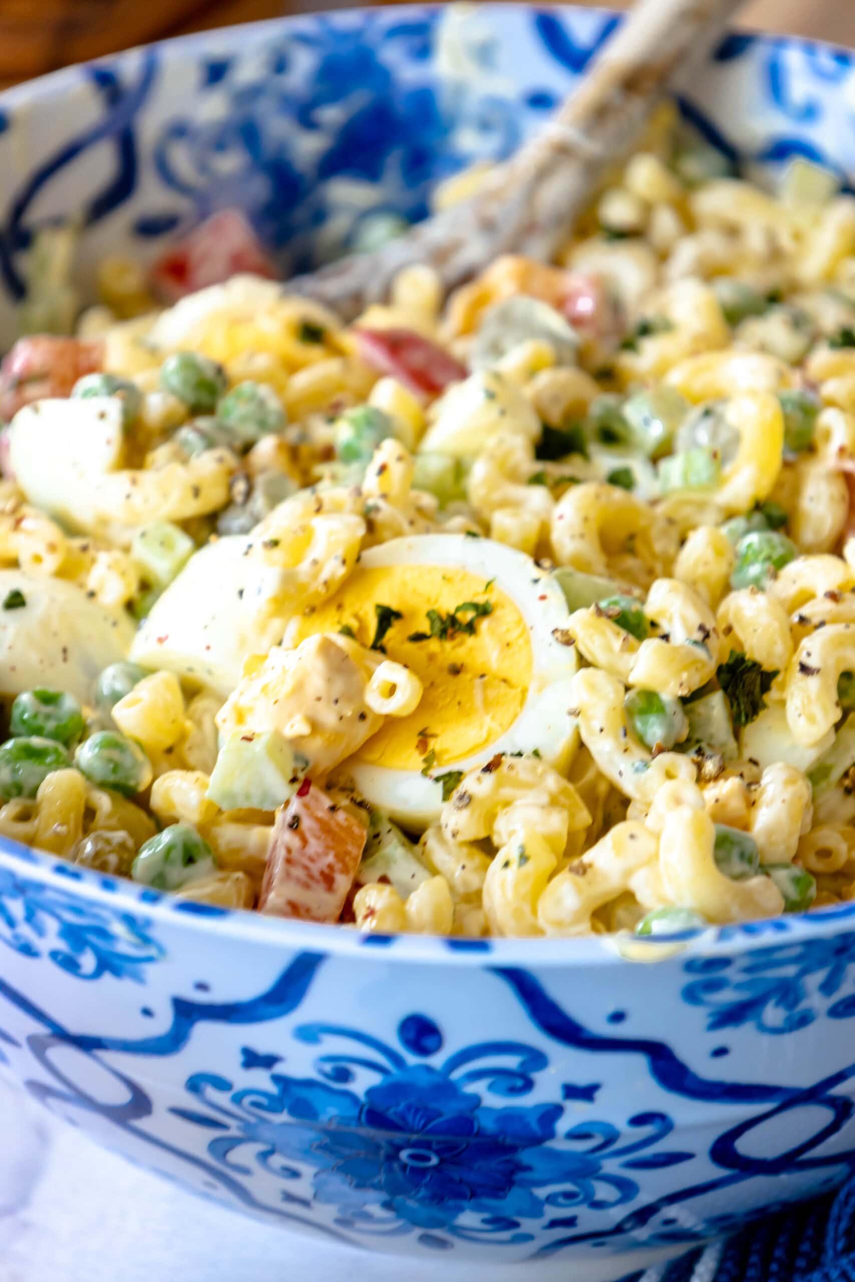 macaroni salad with peppers, peas, mayonnaise, and boiled eggs in a blue bowl