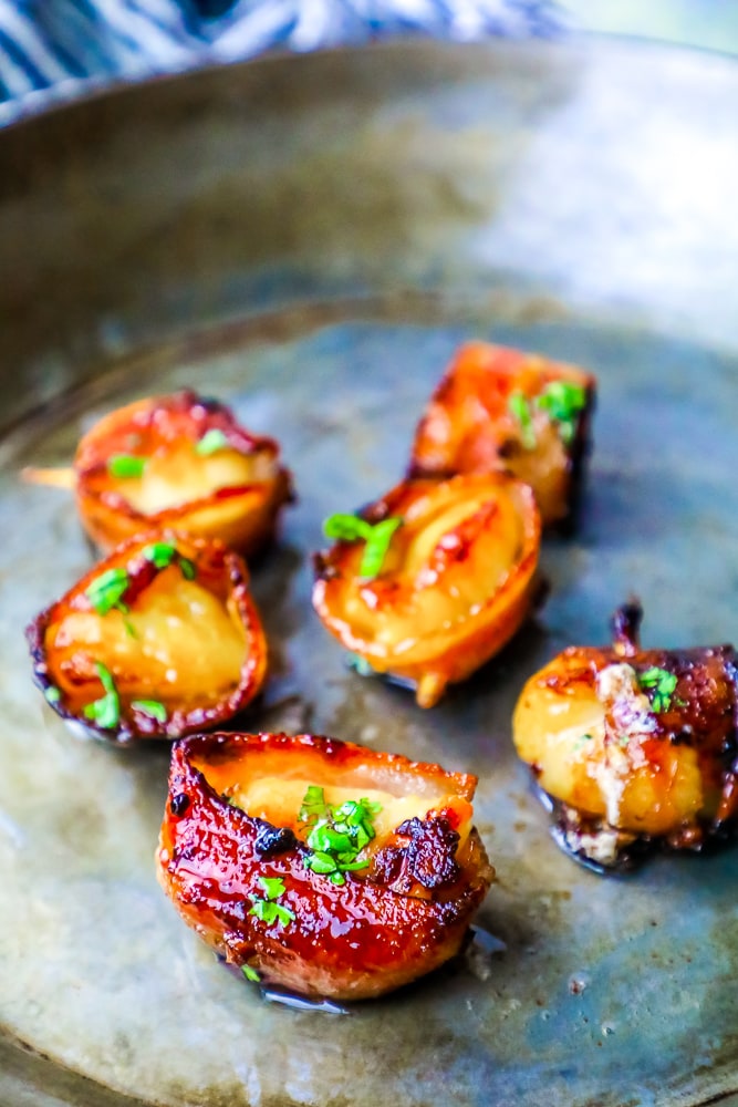 picture of bacon wrapped scallops with a brown sugar glaze on a white plate with chopped parsley on top 