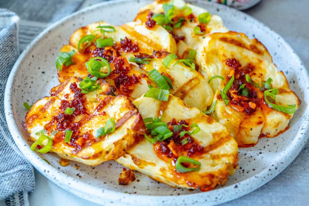 picture of grilled halloumi on a plate topped with spicy garlic, scallions, and honey