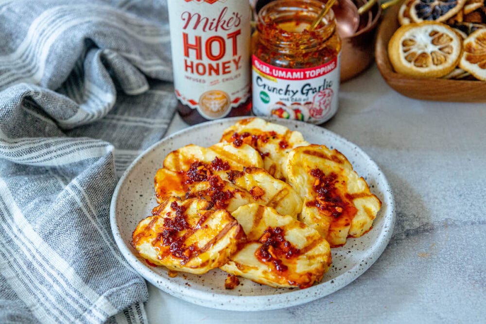 picture of grilled halloumi on a plate topped with spicy garlic, scallions, and honey