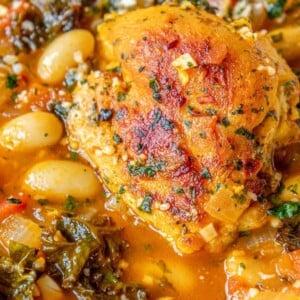 picture of chicken thigh in tomato stew with white beans, kale, herbs, and onions in a white bowl