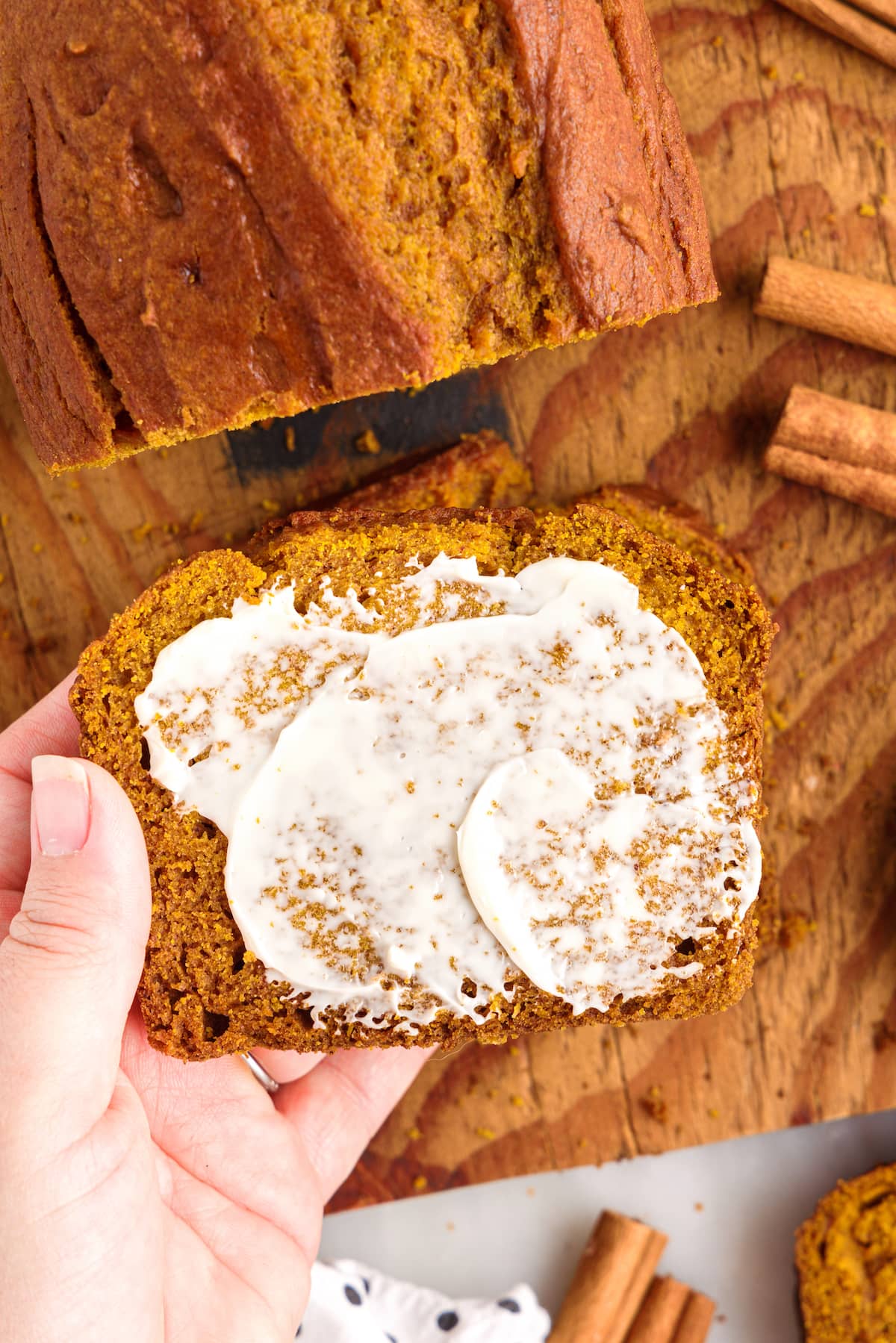 picture of a hand holding a slice of pumpkin bread with butter slathered over it 