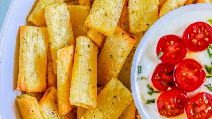 picture of air fryer pasta chips in a bowl with a bowl of feta dip topped with sliced cherry tomatoes in the middle