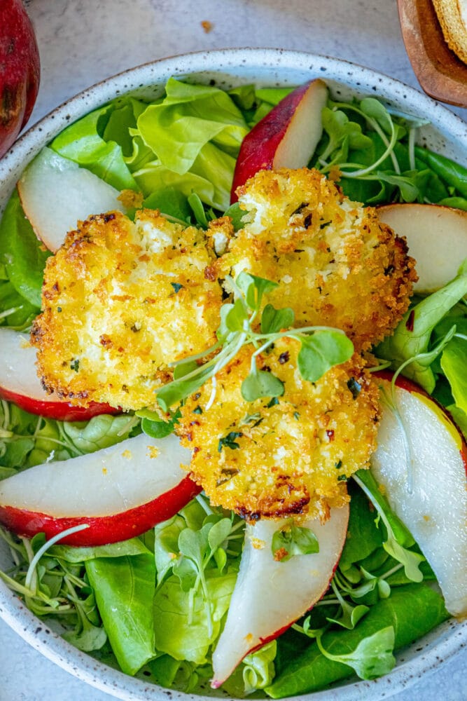 picture of butter lettuce salad with sliced pears and goat cheese balls with champagne vinaigrette dressing on top 