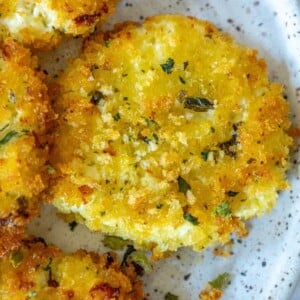 picture of golden baked panko covered goat cheese balls on a white speckled plate and topped with dried herbs