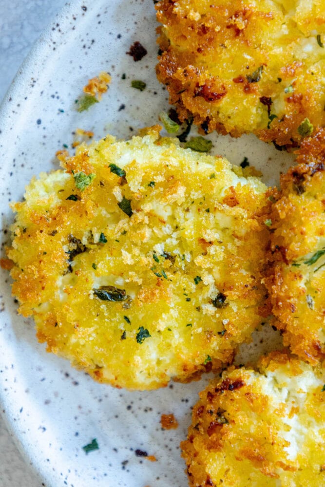 golden baked breaded goat cheese balls topped with herbs on a white speckled plate