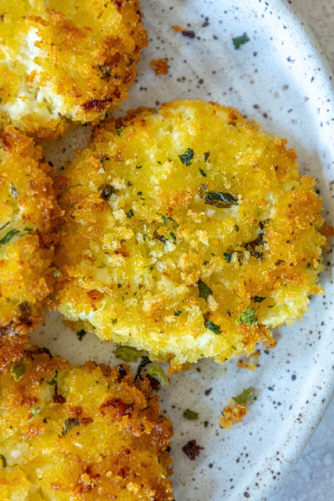 golden baked breaded goat cheese balls topped with herbs on a white speckled plate