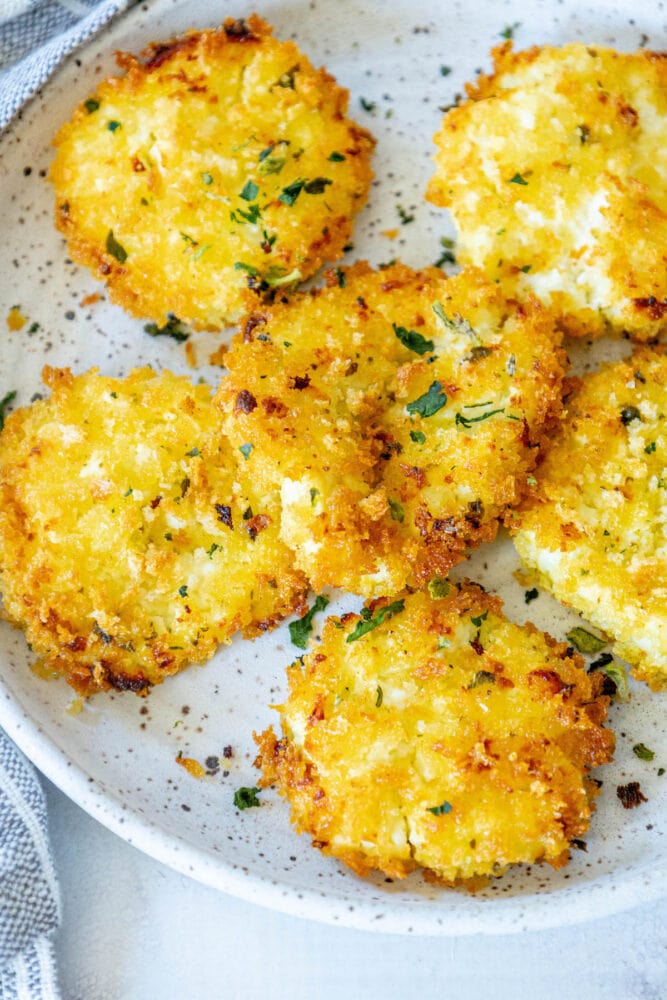 golden baked breaded goat cheese balls topped with herbs on a white speckled plate