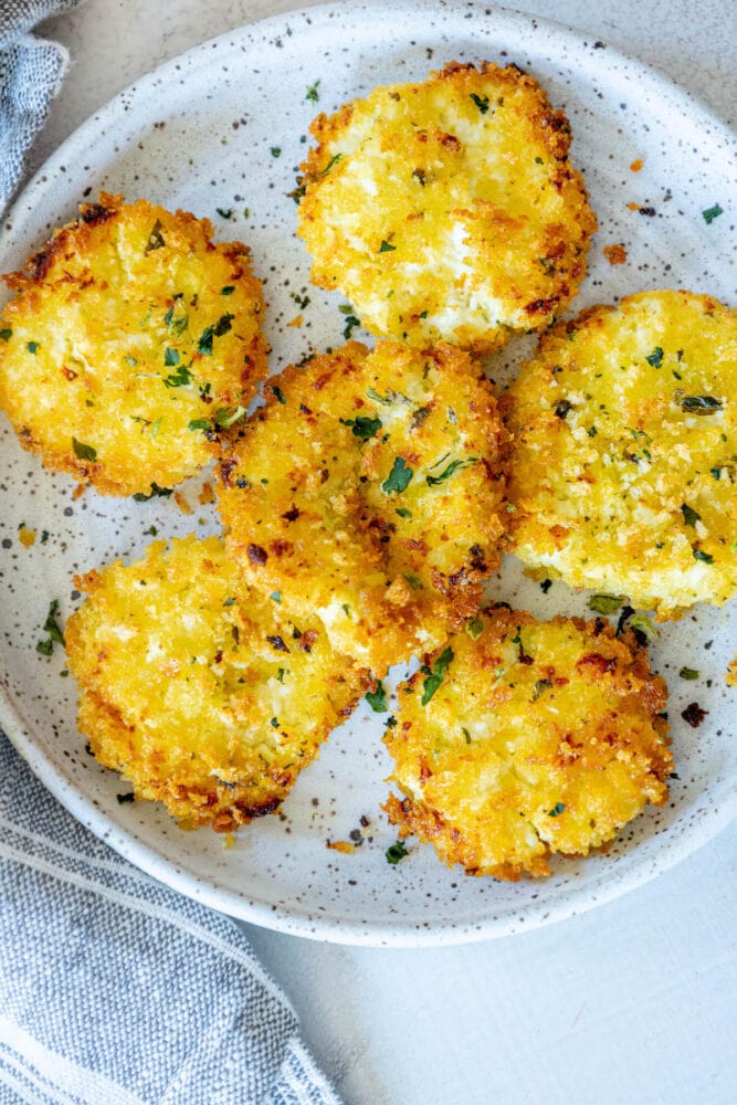 golden baked breaded goat cheese balls topped with herbs on a white speckled plate