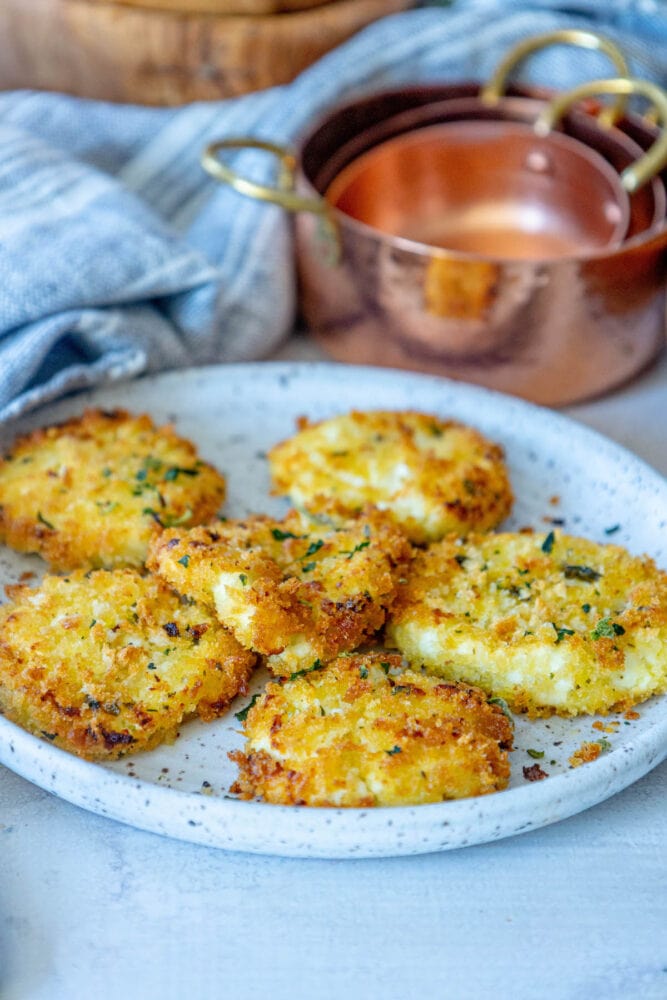 golden baked breaded goat cheese balls topped with herbs on a white speckled plate