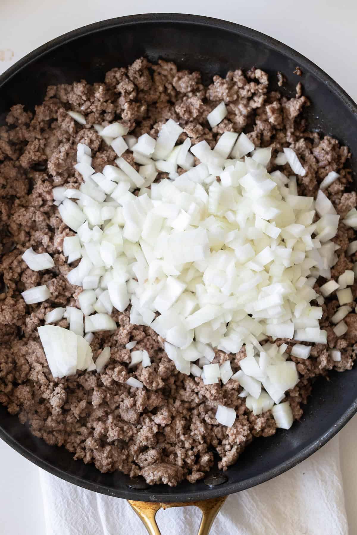 Ground beef cooking in a skillet with chopped white onions on top, perfect for building a flavorful Cheesy Beef Taco Skillet.
