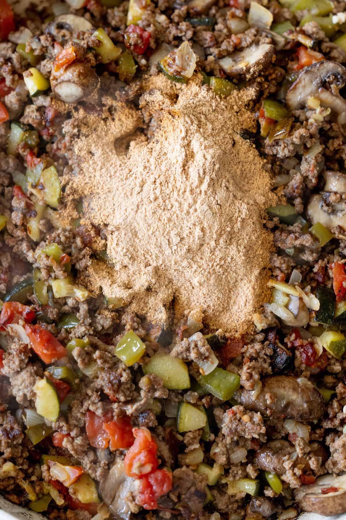 Ground beef, chopped vegetables, and a mound of taco seasoning mix in a pan, ready to be stirred and transformed into the Best Taco Skillet for a flavorful meal.