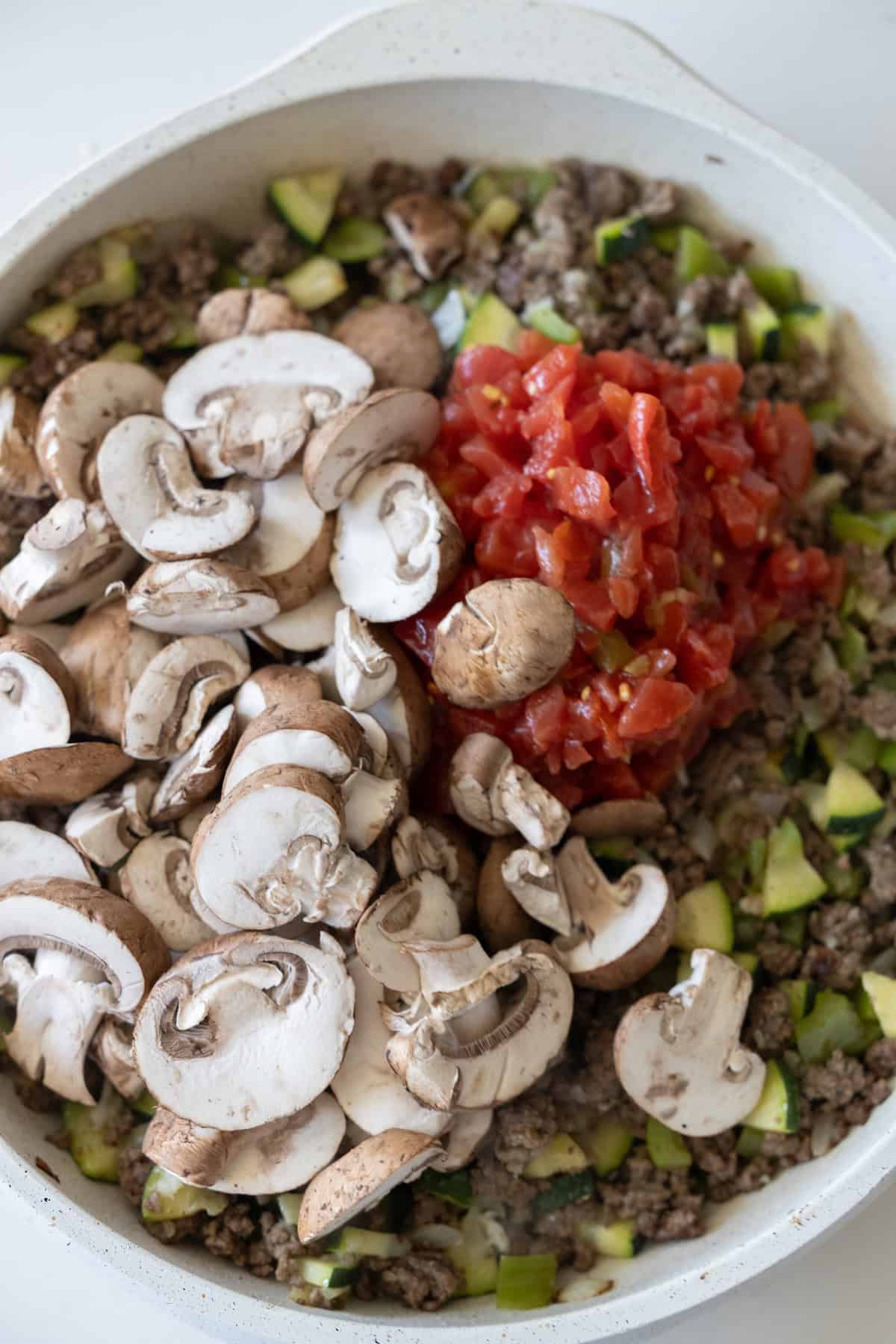 A Cheesy Beef Taco Skillet filled with ground beef, chopped zucchini, uncooked sliced mushrooms, and diced tomatoes.