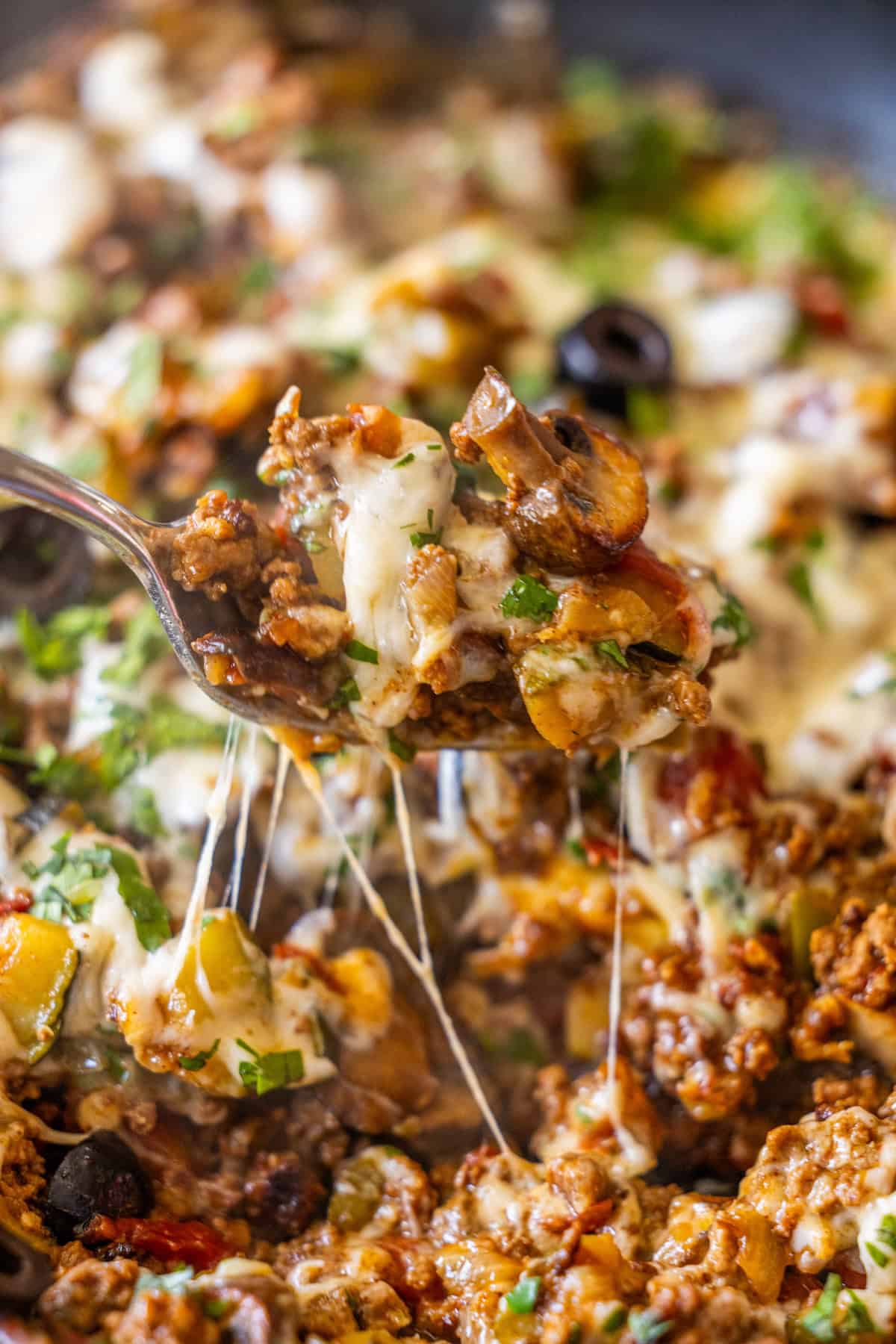 A close-up of a fork lifting a cheesy, cooked ground meat mixture with vegetables and herbs from a Cheesy Taco Skillet.