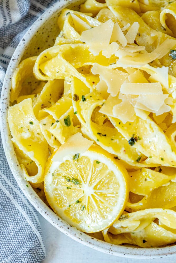 picture of papardelle pasta in a bowl with sliced lemons, garlic, cream sauce, and herbs crumbled on top