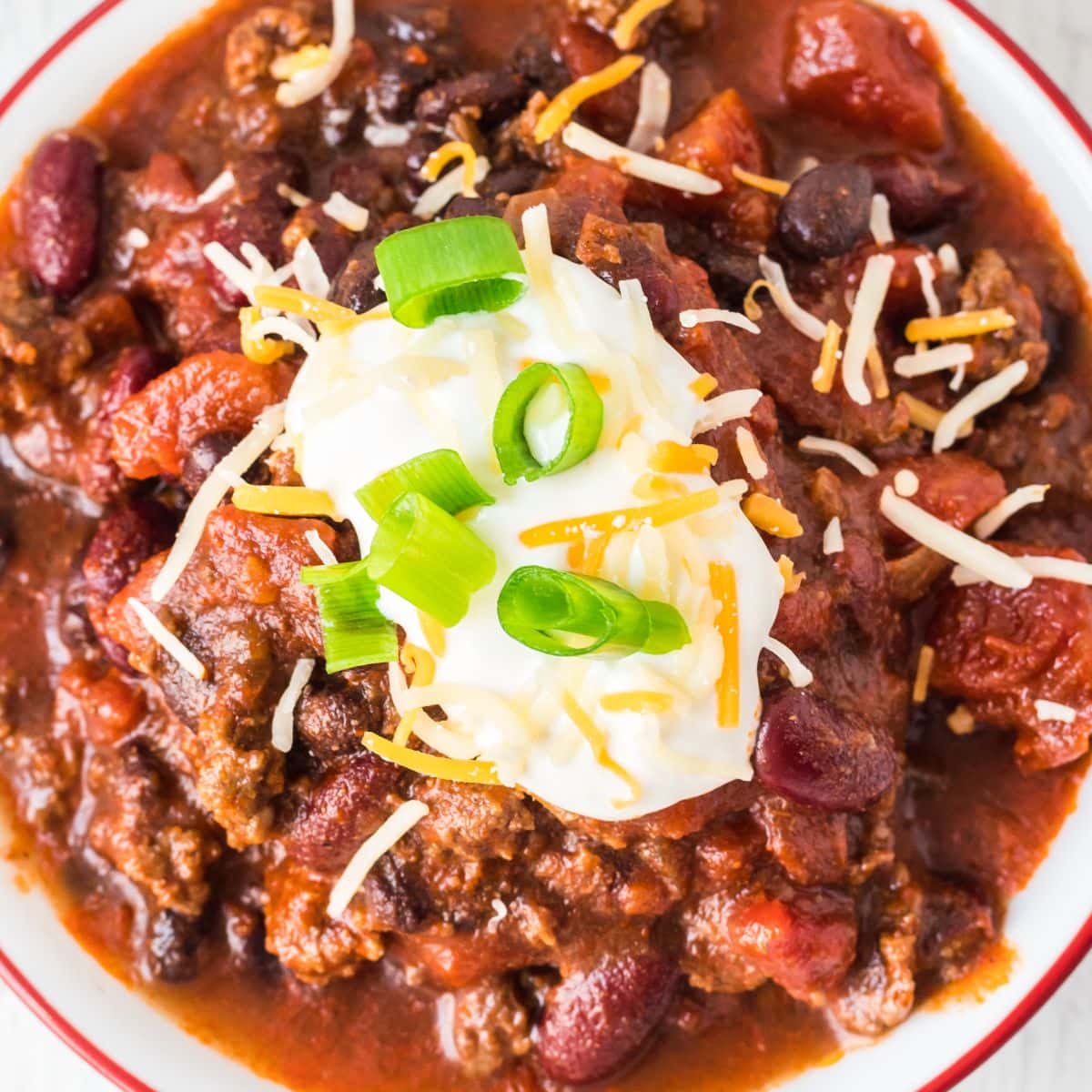 picture of chili in a bowl with sour cream, green onions, and cheese on top