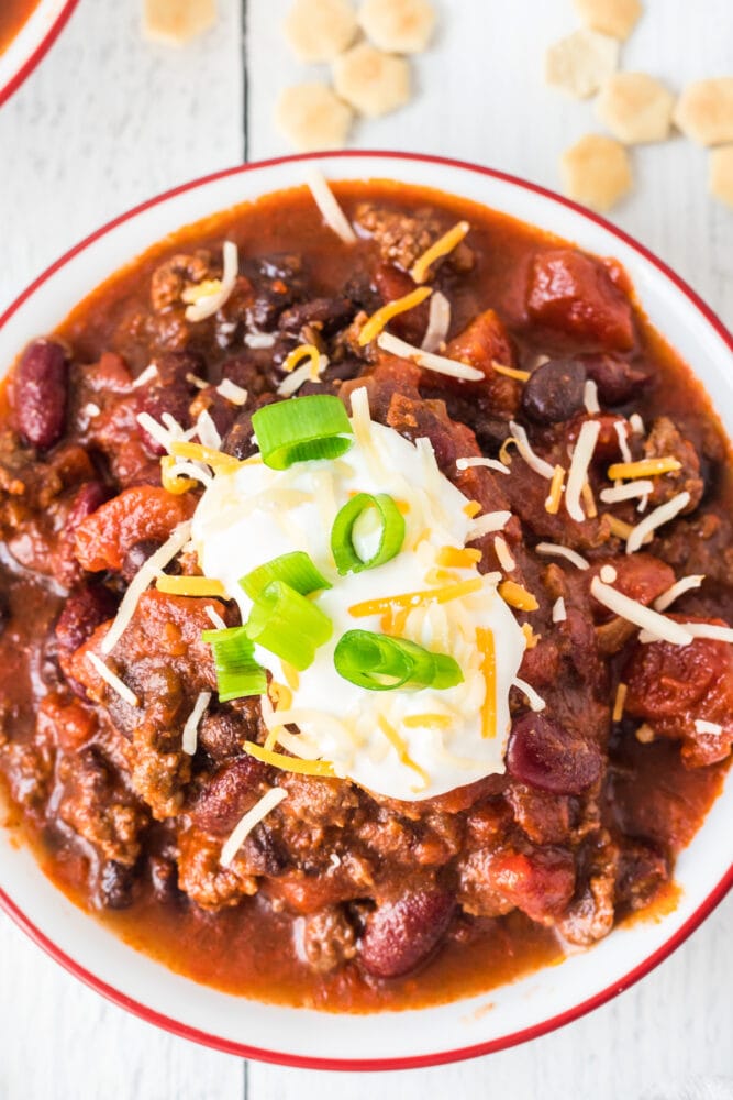 picture of chili in a bowl with sour cream, green onions, and cheese on top 