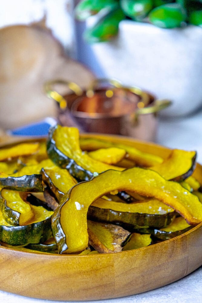 picture of roasted acorn squash slices piled in a wooden bowl seasoned with salt