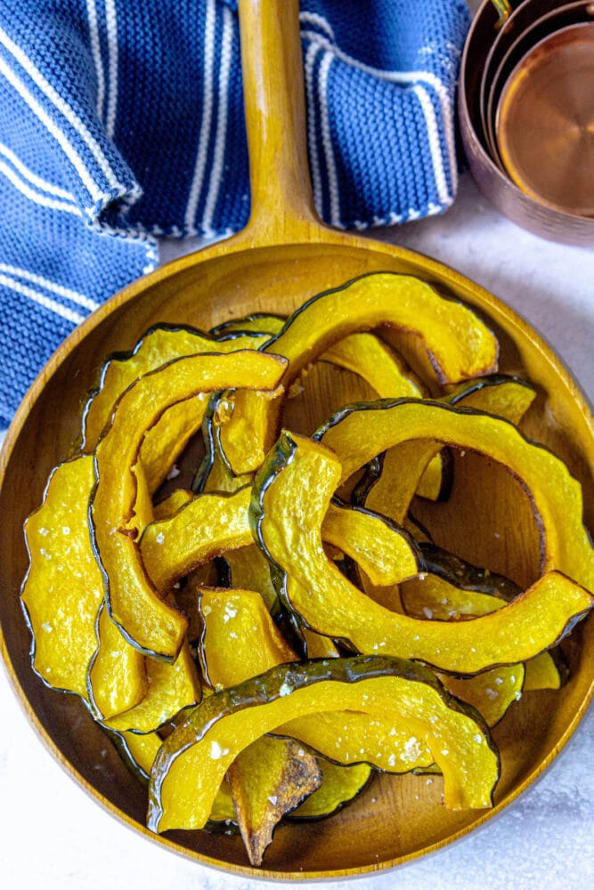 picture of roasted acorn squash slices piled in a wooden bowl seasoned with salt