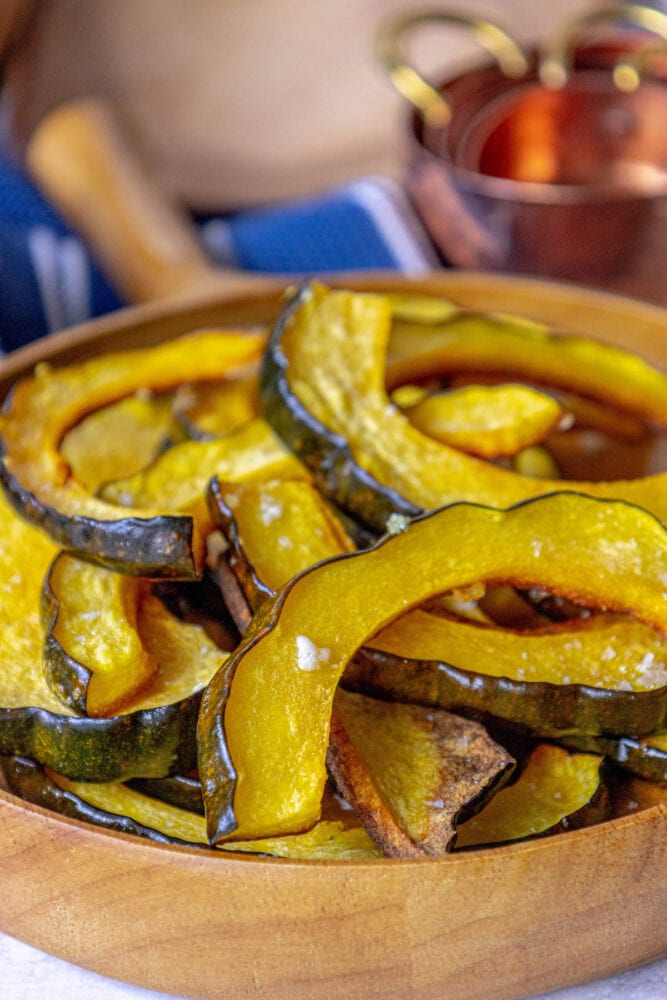 picture of roasted acorn squash slices piled in a wooden bowl seasoned with salt