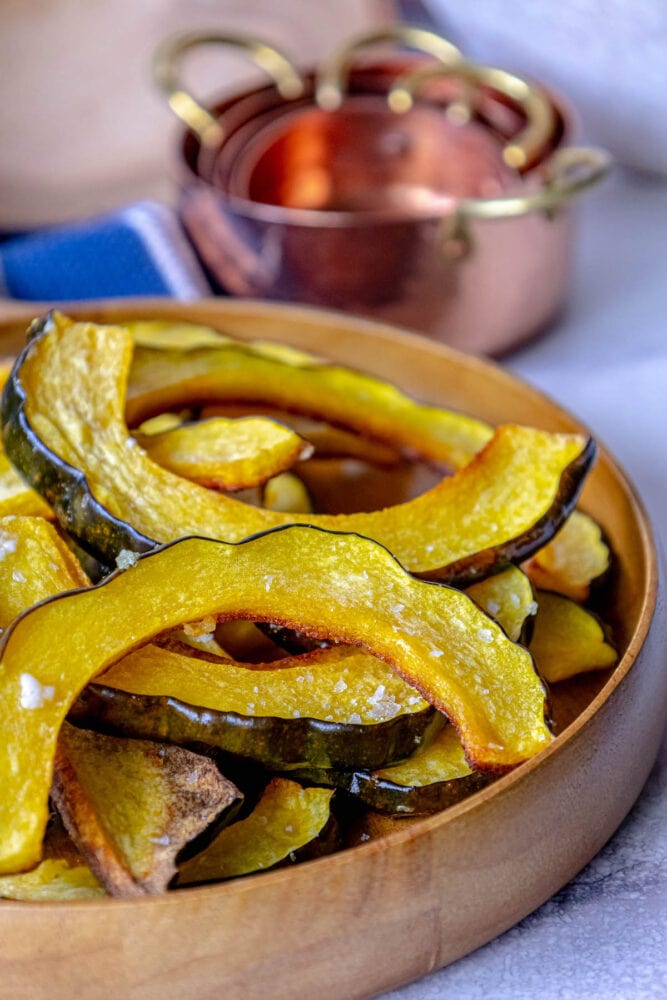 picture of roasted acorn squash slices piled in a wooden bowl seasoned with salt