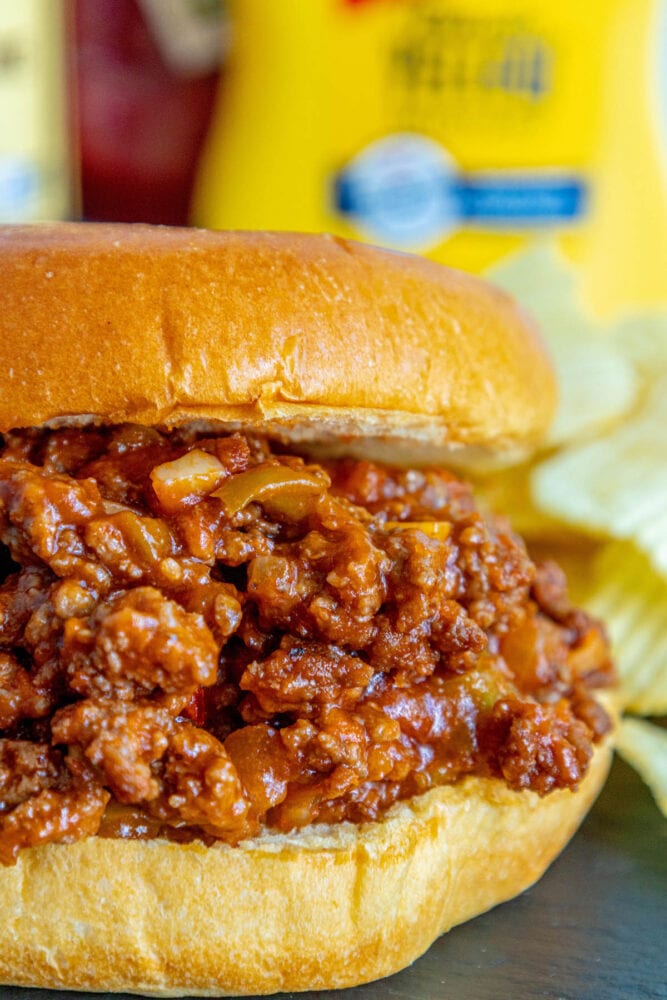 sloppy joe in a bun with lots of sauce on a table