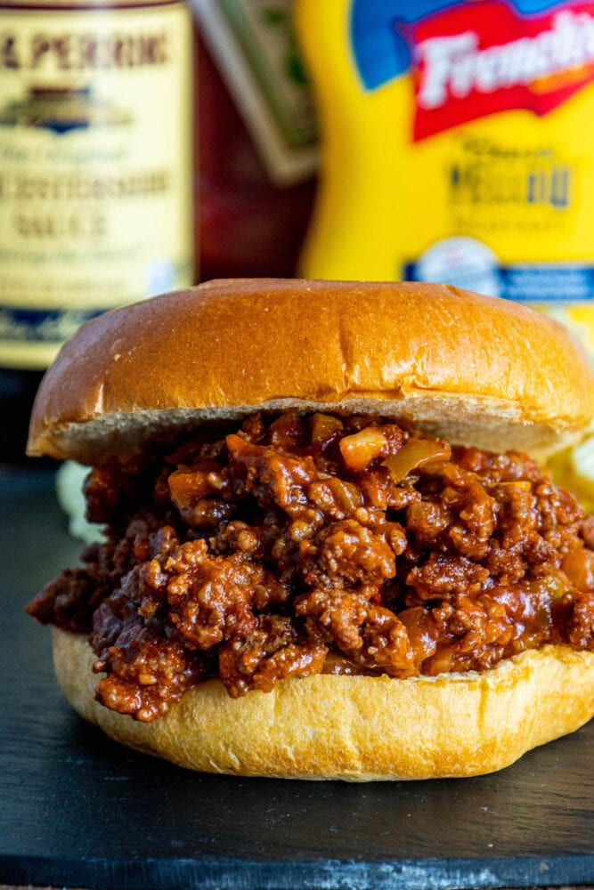 sloppy joe in a bun with lots of sauce on a table