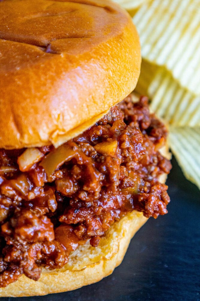 sloppy joe in a bun with lots of sauce on a table