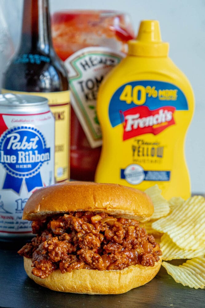sloppy joe in a bun with lots of sauce on a table