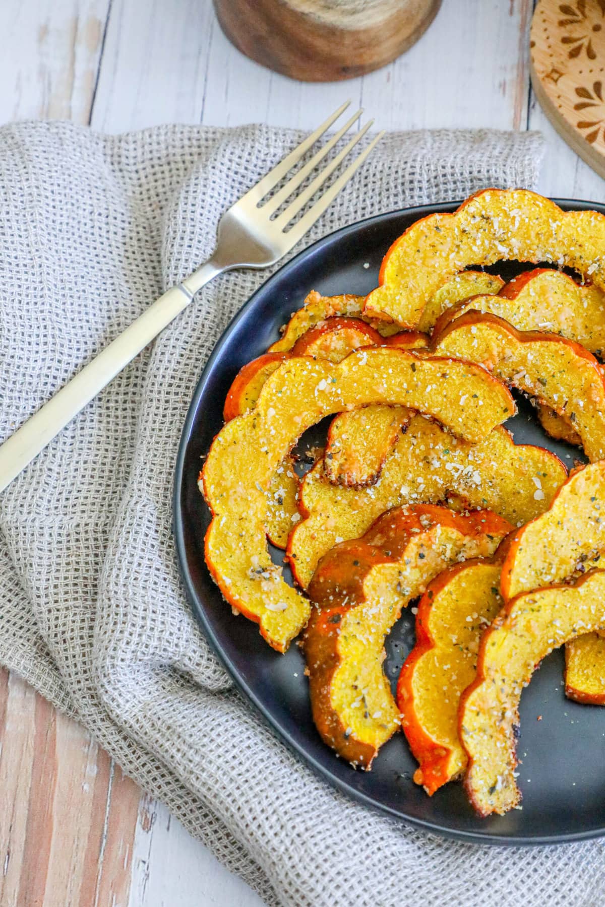 picture of roasted acorn squash slices seasoned with herbs and spices on a black plate