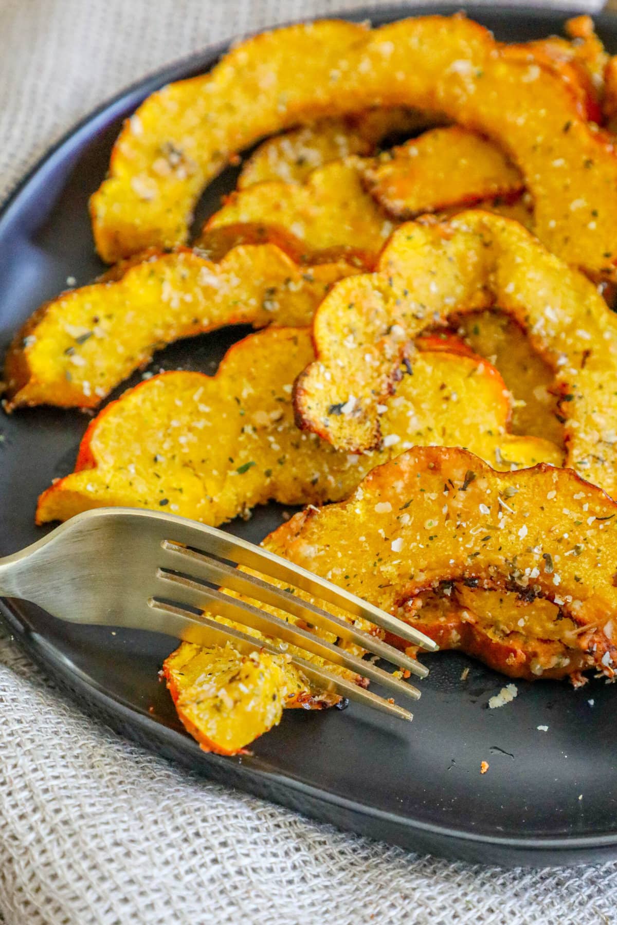 picture of roasted acorn squash slices seasoned with herbs and spices on a black plate