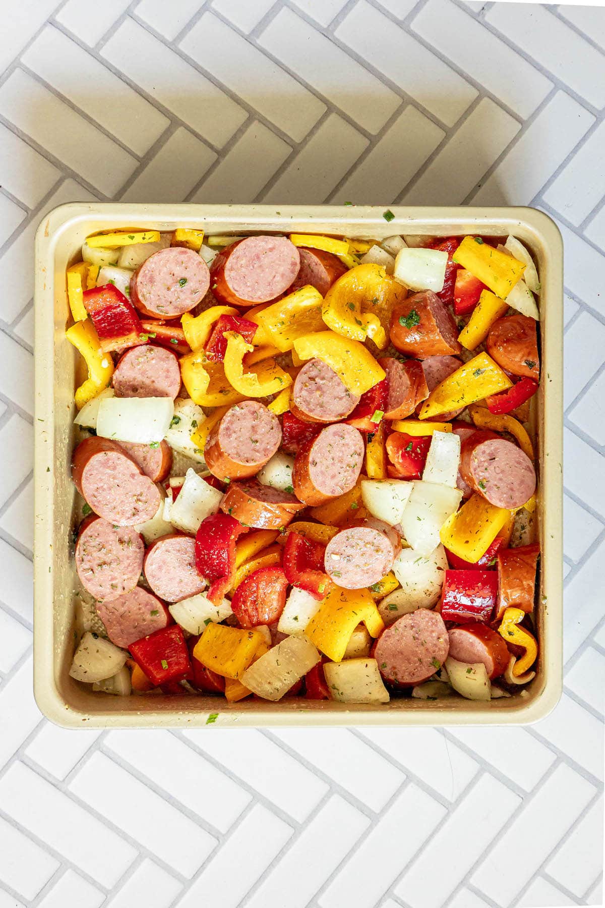 picture of sliced bell peppers, onions, and turkey kielbasa tossed in herb dressing in a pan