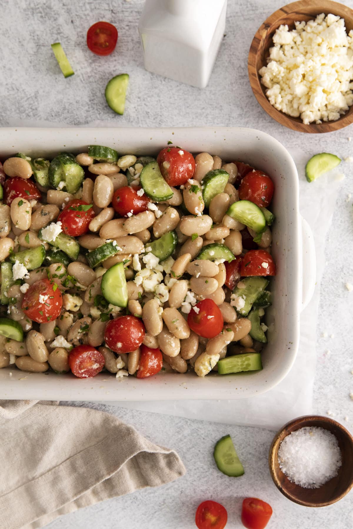  white bean salad in a white bowl with cucumber, tomatoes, and crumbled cheese