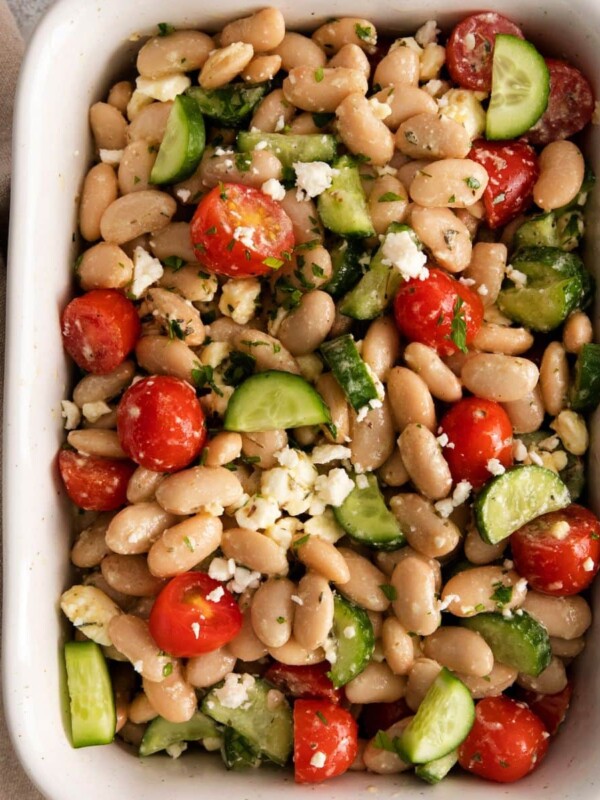white bean salad in a white bowl with cucumber, tomatoes, and crumbled cheese