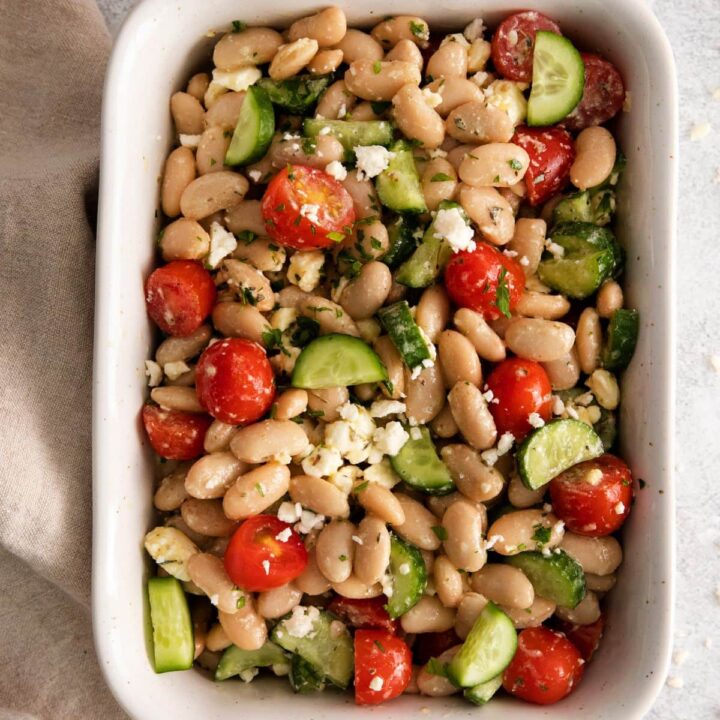 white bean salad in a white bowl with cucumber, tomatoes, and crumbled cheese