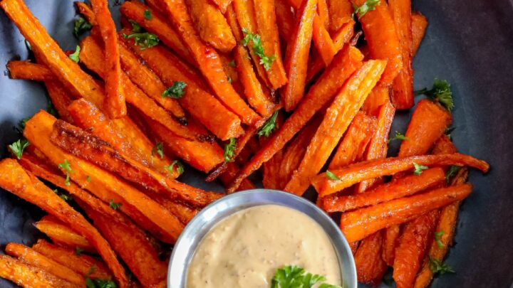 picture of carrot fries on a black plate topped with diced parsley