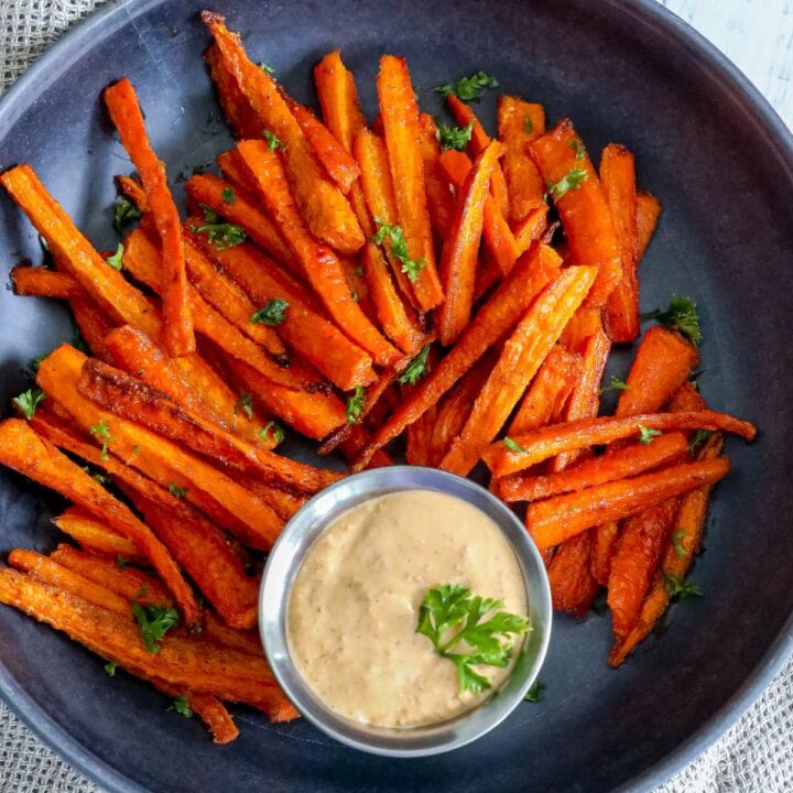 picture of carrot fries on a black plate topped with diced parsley