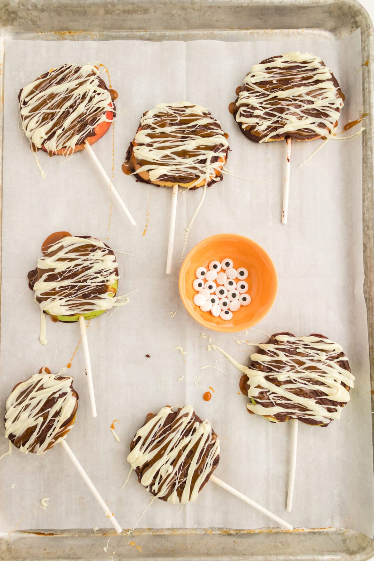 picture of apple slices decorated with chocolate and caramel to look like mummies with candy eyes on a table