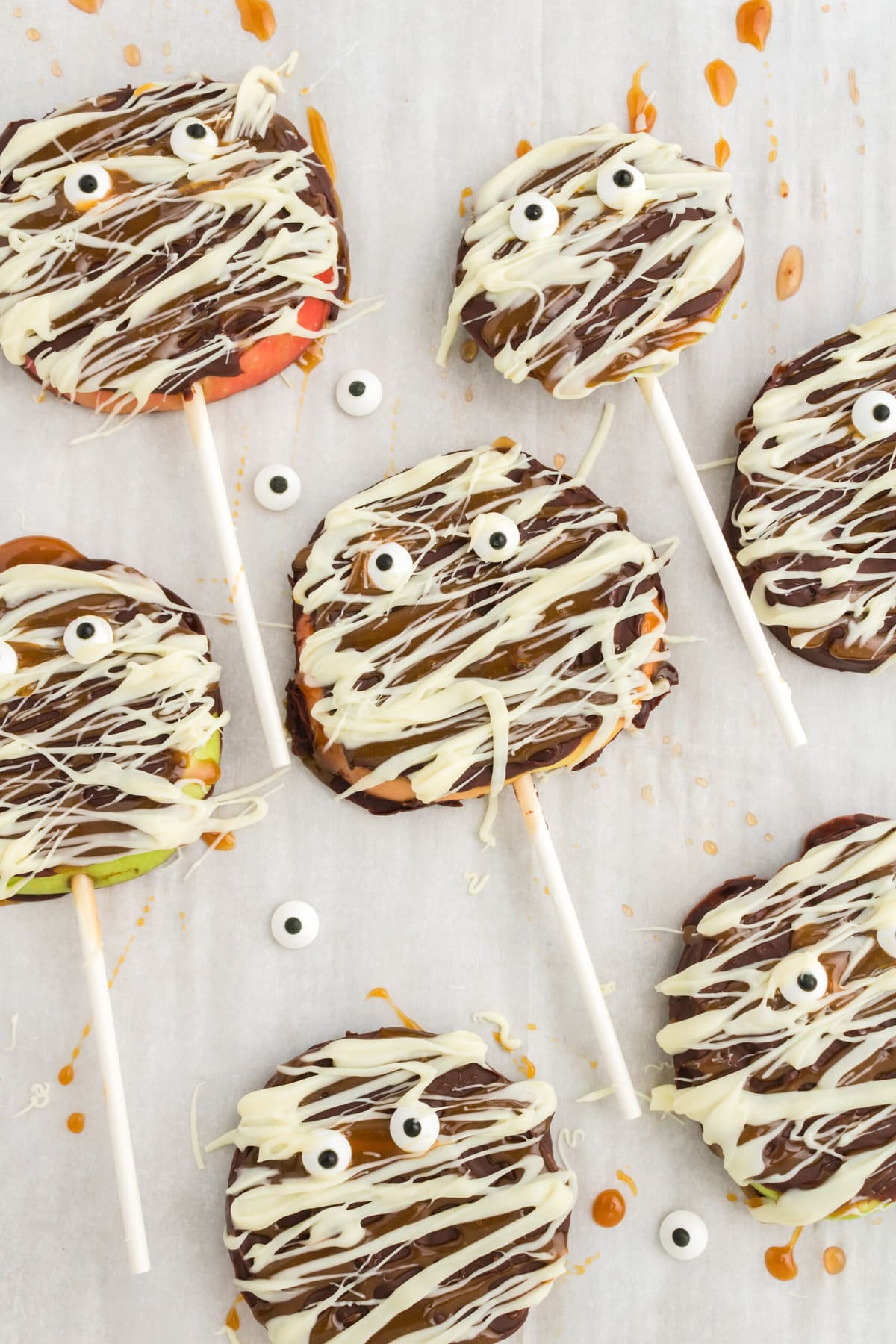 picture of apple slices decorated with chocolate and caramel to look like mummies with candy eyes placed on top on a baking sheet lined with parchment paper
