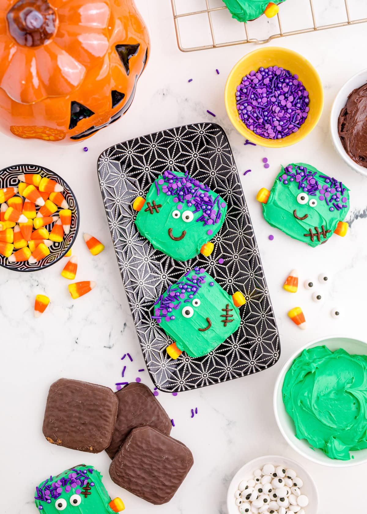 picture of chocolate dipped cookies, covered in green icing with purple sprinkles for hair, candy corn neck bolts, candy eyes, and an icing smile to look like frankenstein