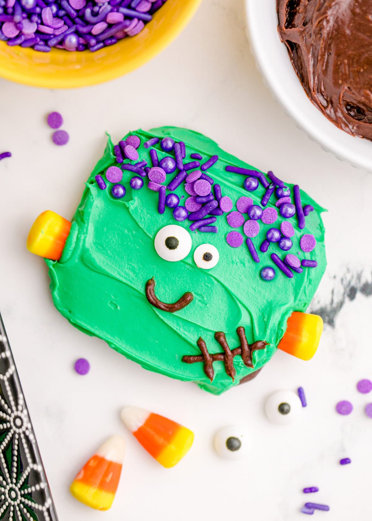 picture of chocolate dipped cookies, covered in green icing with purple sprinkles for hair, candy corn neck bolts, candy eyes, and an icing smile to look like frankenstein