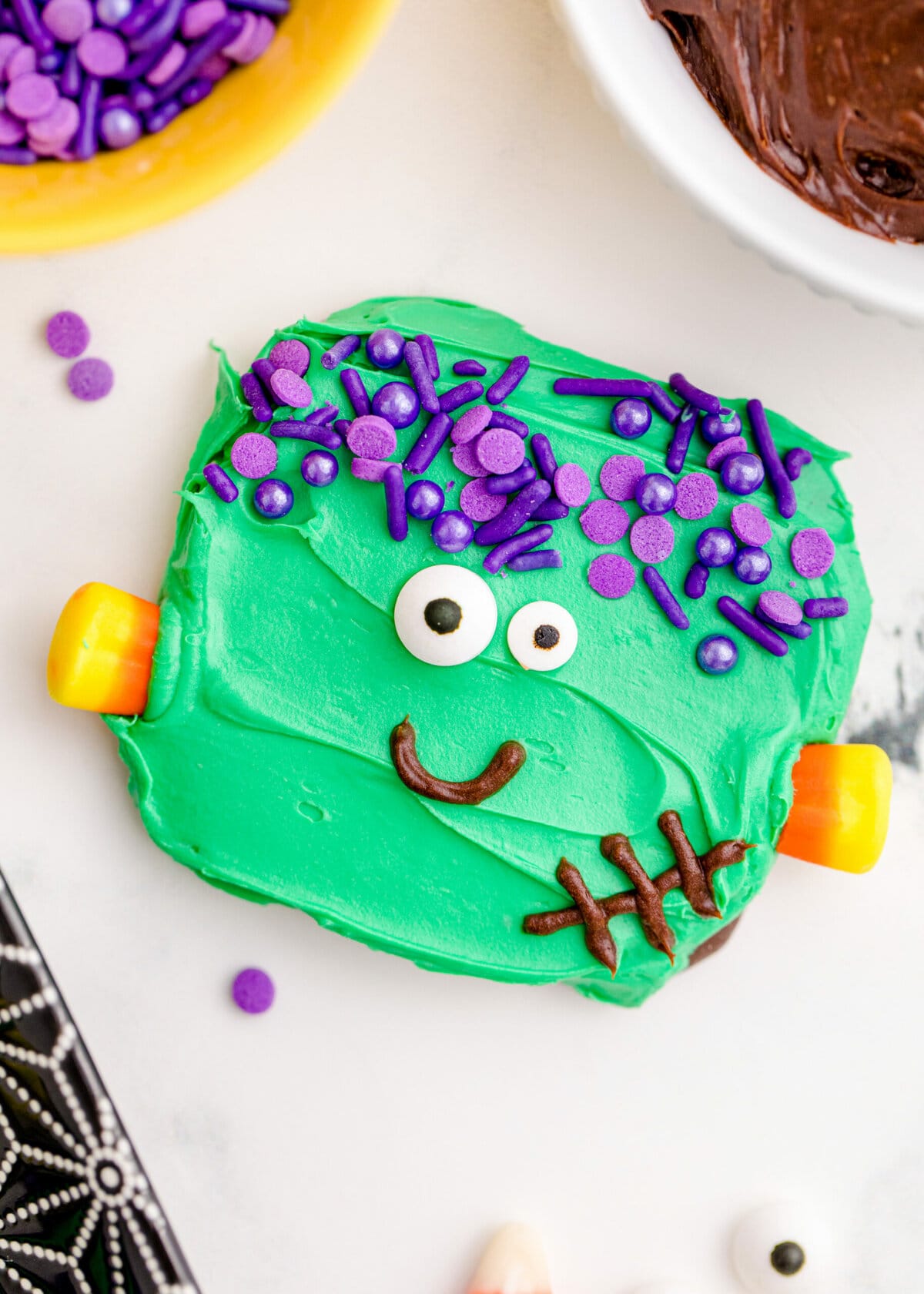 picture of chocolate dipped cookies, covered in green icing with purple sprinkles for hair, candy corn neck bolts, candy eyes, and an icing smile to look like frankenstein