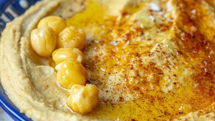 picture of hummus topped with sumac, chickpeas, and olive oil in a blue bowl