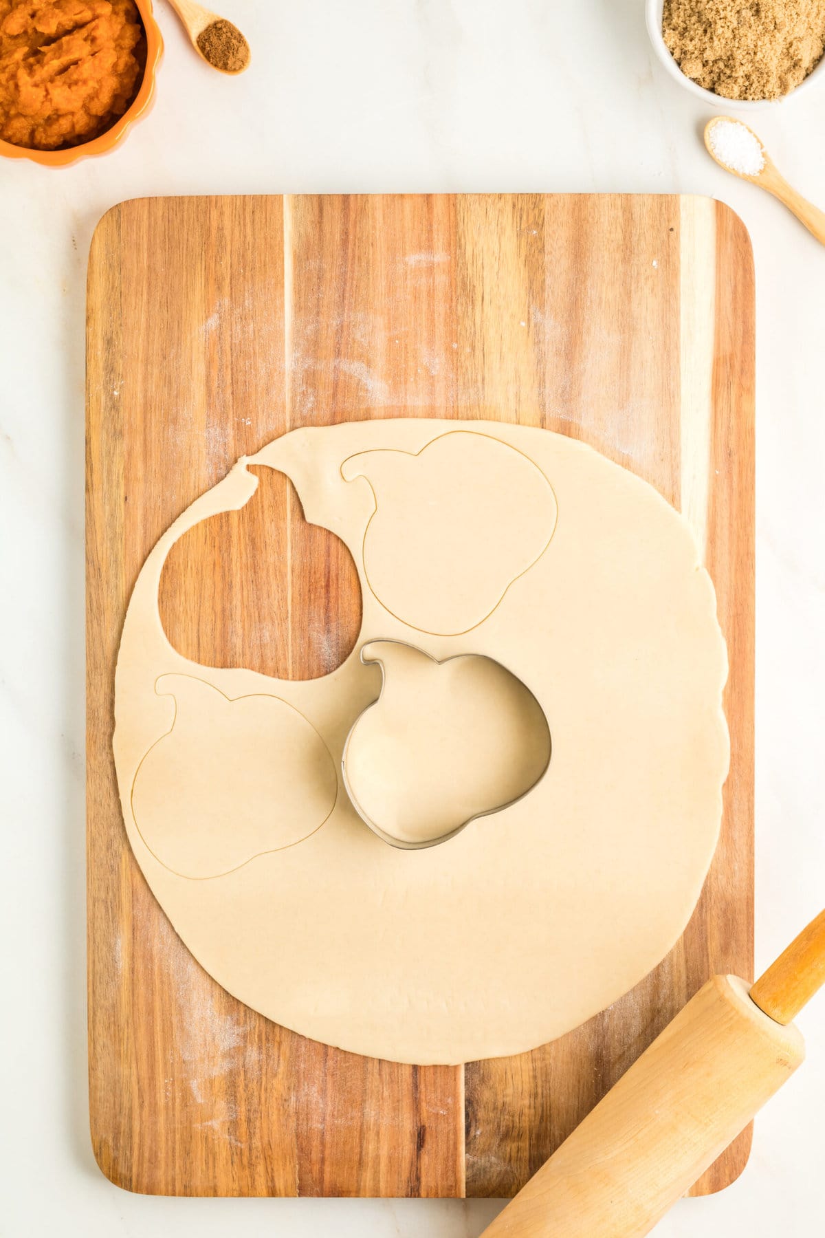 picture of dough on a cutting board with pumpkin cookie cutter cutting a pumpkin shape out of the dough