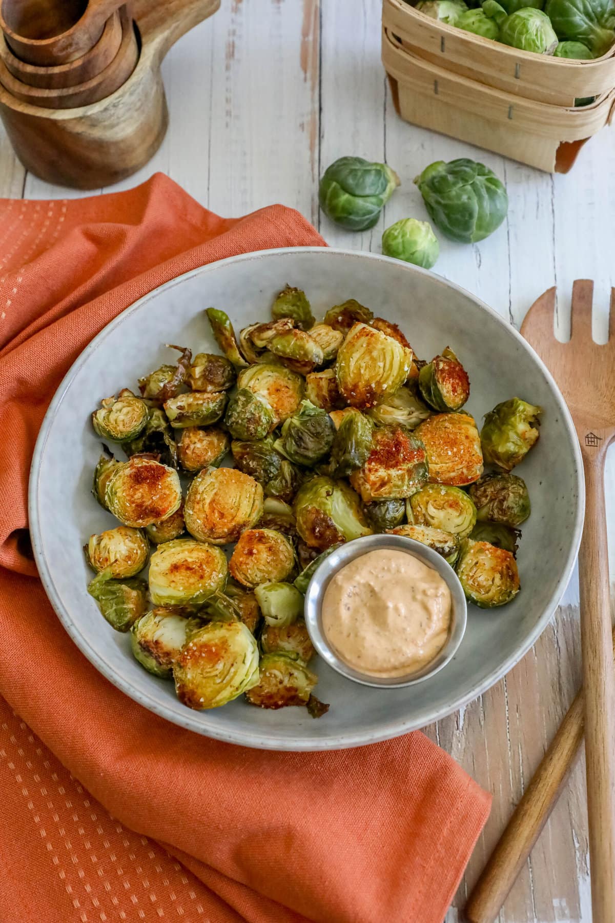 picture of garlic roasted brussels sprouts in a white bowl with a cup of sauce