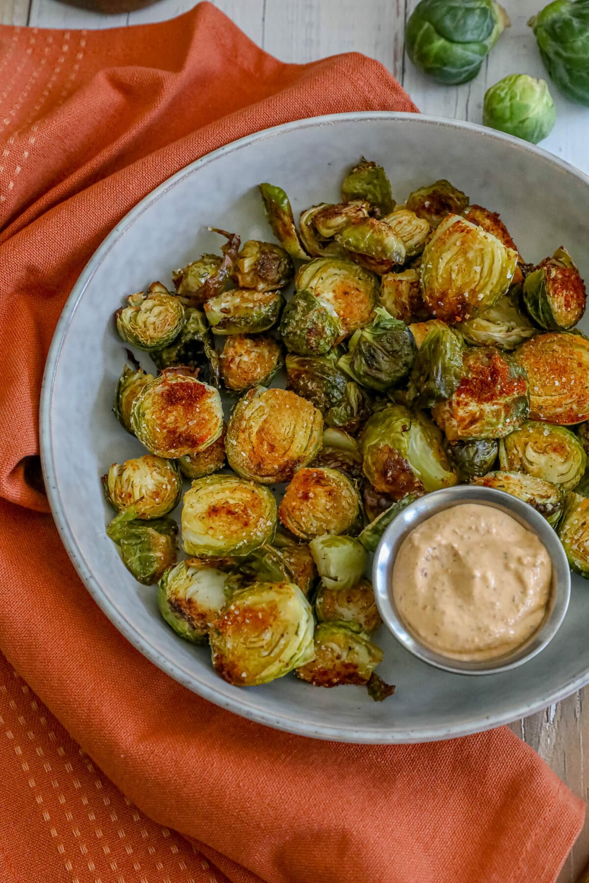 picture of garlic roasted brussels sprouts in a white bowl with a cup of sauce